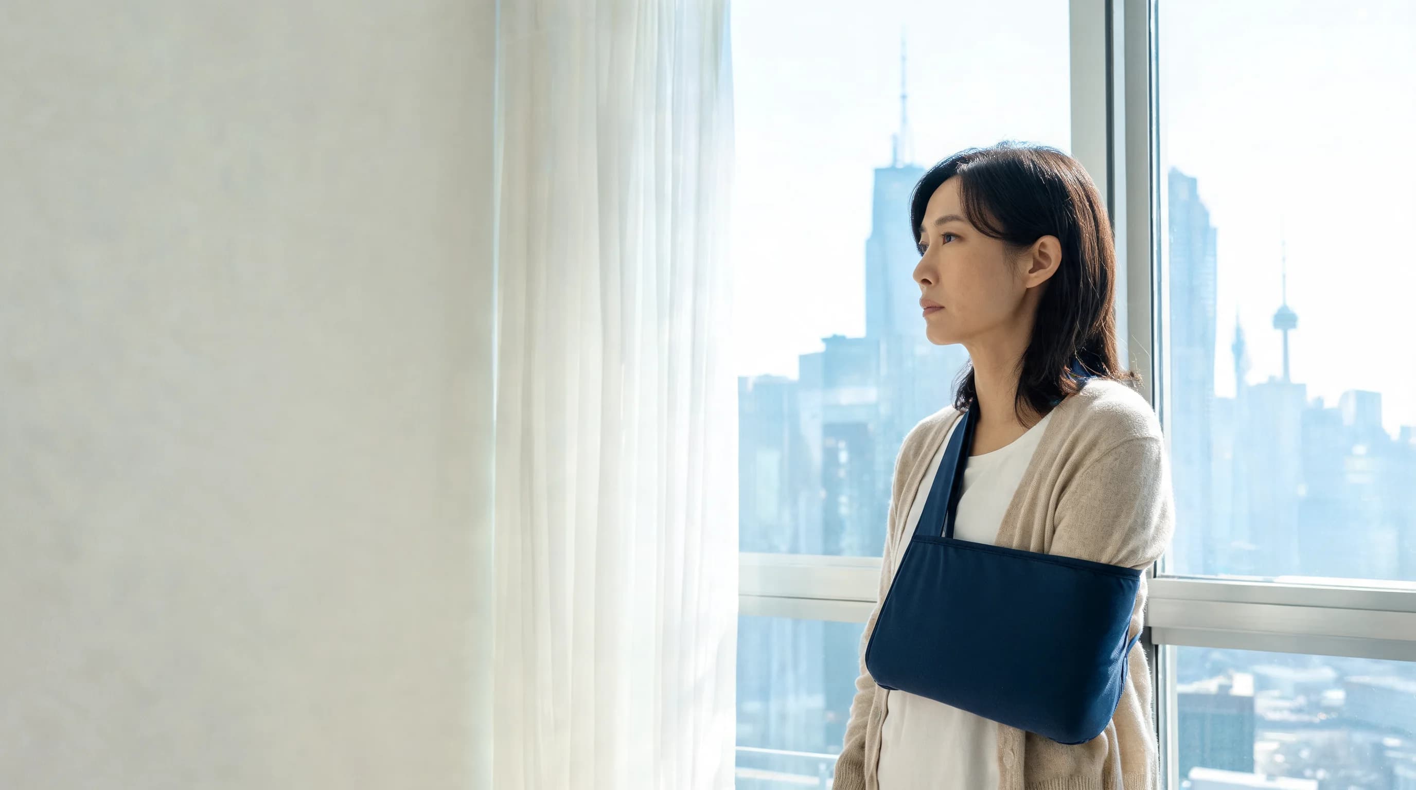 다친 팔을 보호대로 감싸 목에 건 채 토론토 시내가 내려다보이는 콘도 창가에 서 있는 한인 여성